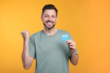 Happy man holding condom on orange background