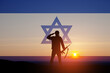 © hamara - Silhouette of soldier saluting against the sunrise in the desert and Israel flag.