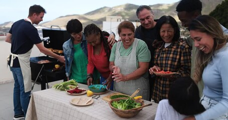 Wall Mural - Multi generational people doing barbecue during weekend day at home's rooftop preparing vegetable food - Multiracial friends having fun cooking together - Summer and food concept