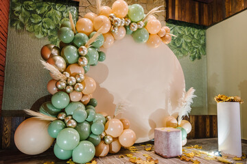 Arch decorated green, brown, golden balloons, dry autumn leaves for wedding ceremony. Celebration baptism. Trendy autumn decor. Reception at birthday party. Photo wall decoration space, place for text