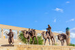 Sculpture composition of Caravan with drover and camels on the old town wall of Ichan-Kala. Khiva (Xiva), ancient city at Silk Road. Uzbekistan. Blue sky, copy space