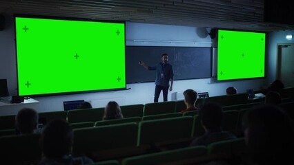 Poster - Young University Professor Explaining a Lecture, Pointing on a Green Screen Mock Up Display. Group of Diverse Multiethnic Students Study in a Dark Auditorium. Teacher Showing Content on Big Screens