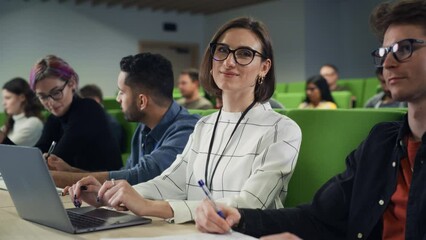 Poster - Portrait of a Happy Young Caucasian Female in Glasses Looking at Camera and Smiling. Young Female Student Using Laptop Computer and Studying in University with Diverse Multiethnic Classmates