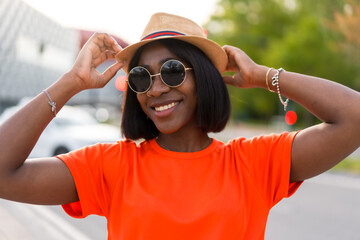 Portrait of young black woman with sunglasses and hat, wearing orange t-shirt, enjoying summer in the city, lifestyle photos