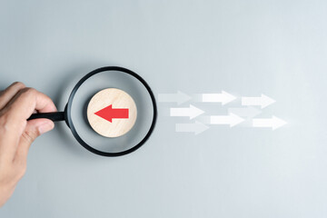 Aufkleber - Hand holding magnifier focus to Red arrow and different direction facing opposite direction with white arrow for business disruption and technology transformation and different thinking idea concept.