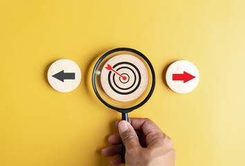 Fototapete - Hand holding magnifier focus to dardboard with Red arrow and different direction facing opposite direction with black arrow for business disruption and technology transformation.