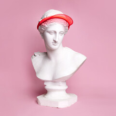 Antique statue bust wearing stylish cap against pink background. Sportive look, hobby, active lifestyle. Concept of creativity, modernity and vintage, antique art. Inspiration and imagination