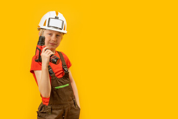 Poster - Child wears helmet and working overalls holds drill in his hands. Boy 9-10 years old imitates builder, yellow background. Copy space