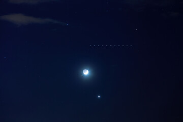 Flying Starlink satellite in dark night cloudscape. Night sky with crescent moon, stars, bright Venus and group of Starlink satellites