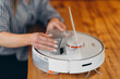 A young beautiful woman is cleaning a smart robot vacuum cleaner from dust.