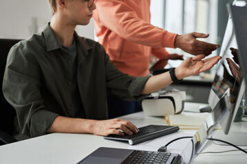 Close-up of two programmers pointing at monitor and discussing presentation on computer while working at table in team