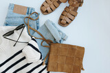 Fototapeta Kawa jest smaczna - Trendy stylish fashion collage with female clothes and accessories: leather sandals, suede shoulder bag, blue jeans, striped sweater on white background with copyspace. Flat lay, top view