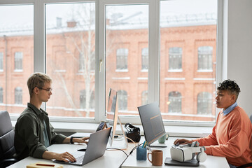 Young programmers sitting at table in front of computers and typing computer codes for software during work in IT office
