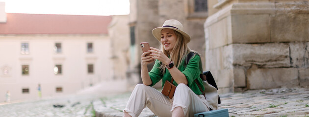 Poster - Young woman travel alone in old city centre, sitting and using smartphone.