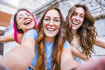 Group of young women friends taking selfie shot with smartphone while smiling -Three happy multiracial girls having looking at camera outdoors at city-Cheerful Friendship and Diversity Concept 