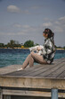A girl with a white dog sits on a wooden pier on the shore of a lake, on a sunny day.