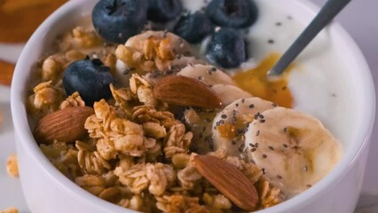 Wall Mural - Bowl of oat granola with yogurt, banana, blueberries, chia seeds, honey and nuts on white background for healthy breakfast. Close up Generative AI