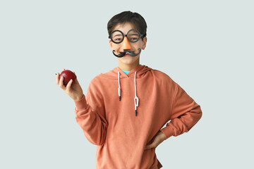 Poster - Little boy in funny disguise with apple on light background. Children's Day celebration