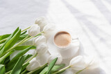 Fototapeta Tulipany - Cozy morning coffee cup with white tulip flowers from above, breakfast on Mothers day or Womens day. Top view with copy space Floral composition Romantic background