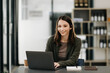 © Nuttapong punna - Business Caucasian woman Talking on the phone and using a laptop with a smile while sitting at modern office