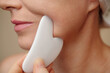 © DragonImages - Closeup image of middle-aged woman using gua sha when massaging lower part of her face