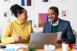 © Studio Marmellata - Positive Ethiopian coworkers in smart casual clothes sitting at table near laptop and discussing project details during workday in office