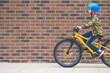 Profile view of boy in helmet riding bike on sidewalk against background of brick wall