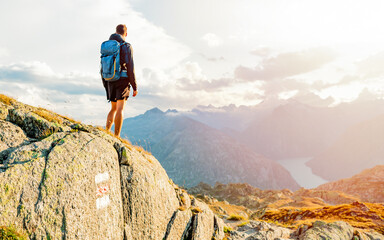 Wall Mural - Man traveler with backpack standing on top of the mountain and looks into the distance. Freedom concept. Filtered image:cross processed instagram and soft focus effect.