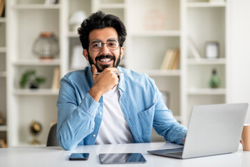 Successful Freelancer. Happy Handsome Indian Man Posing At Desk With Laptop Generative AI