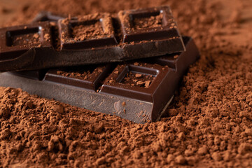 Dark and milk chocolate with nuts on a dark background sprinkled with cocoa powder.