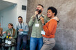 © Mediteraneo - Business people singing karaoke in modern office