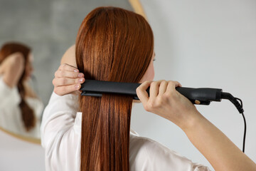 Beautiful woman using hair iron in room