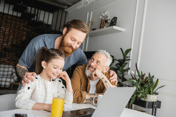 Wall Mural - Smiling homosexual man hugging daughter and partner near devices and notebooks at home. 