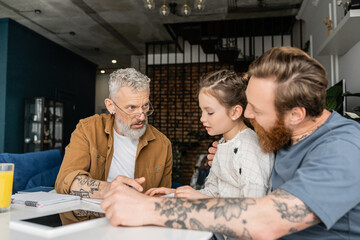 Wall Mural - Preteen girl doing homework with homosexual parents near digital tablet at home. 