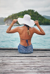 Wall Mural - Look at this view. Rearview shot of an unrecognizable woman sitting on a boardwalk overlooking the ocean during vacation.