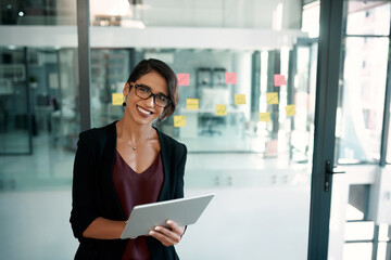 Canvas Print - Welcome to the digital age. Cropped portrait of an attractive young businesswoman standing alone in her office and working on a tablet.