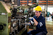 © FotoArtist - Lathe Operators Concentrated on Work. Worker in uniform and helmet works on lathe, factory. Industrial production, metalwork engineering, manufacturing.
