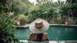 Elegante jovem elegante posando enquanto está sentado perto da piscina. Chapéu, maiô, moda ao ar livre, elegante chapéu preto