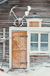 Old rustic house made of timber and covered in snow. The building has a yellow or orange wooden door and a window next to it. Snowy village in Lapland, Finland on a cold winter day.
