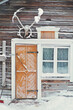 Old rustic house made of timber and covered in snow. The building has a yellow or orange wooden door and a window next to it. Snowy village in Lapland, Finland on a cold winter day.