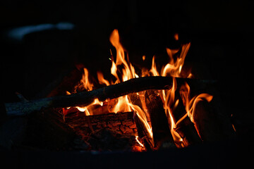 Close-up of a campfire. Fire burning brightly with a big yellow and orange flame in the dark. Firewood and logs burning to ember and ash. Enjoying the warmth of the fire at a cold winter night.