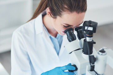 Seeing life at a small scale. a focused young female scientist looking through a microscope while doing tests inside of a laboratory.