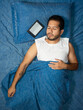© Narayan - young latin man reading an e-reader book on blue bed, electronic e-book concept
