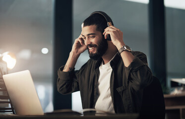 Poster - Music on, lets make it happen. a young businessman using a laptop and headphones during a late night at work.