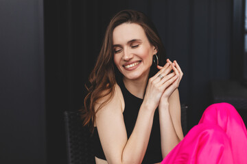 Poster -  Attractive brunette woman sitting at home outdoors, wear pink pants, black top circle earrings. Girl joy of free time, look happy, smiling, look bright. Shot of happy hippie lady isolated black wall.