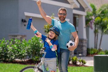 Wall Mural - Sporty family. Excited father and son with winning gesture. Father teaching son riding bike. Fatherhood. Support parent. Fathers day. Child care. Fathers day.