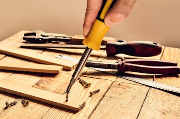 Hand holding tool in the workshop. Screwdriver, flat file, pliers, monkey wrench, screws and boards on natural wooden background.