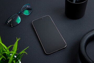 Aufkleber - Phone placed on black desk among office items like a headset, plant, glasses, and a coffee mug