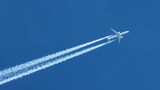 Jet airplane flying overhead in clear blue sky diagonally with condensation trail