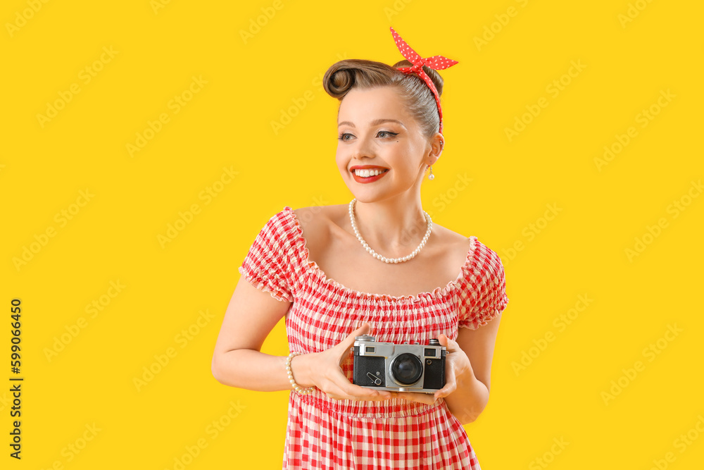 Young pin-up woman with photo camera on yellow background